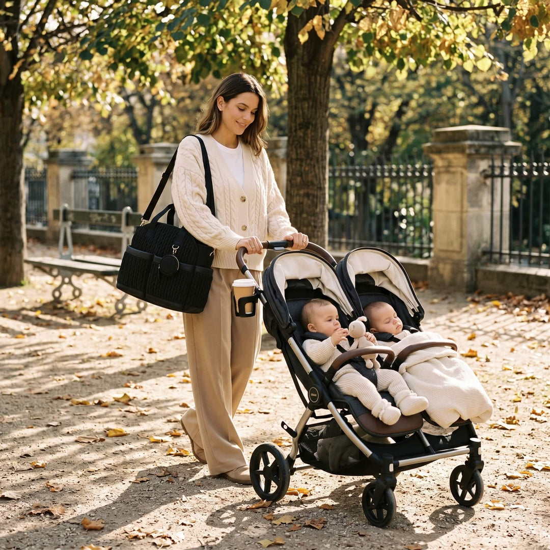 Grand sac à langer porté par une maman de jumeaux poussant une double poussette au parc parisien