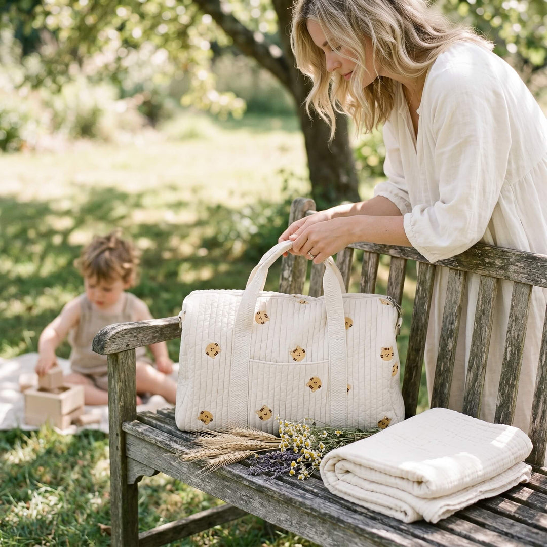 Sac à langer en gaze de coton naturelle posé sur un banc en bois dans un jardin ensoleillé